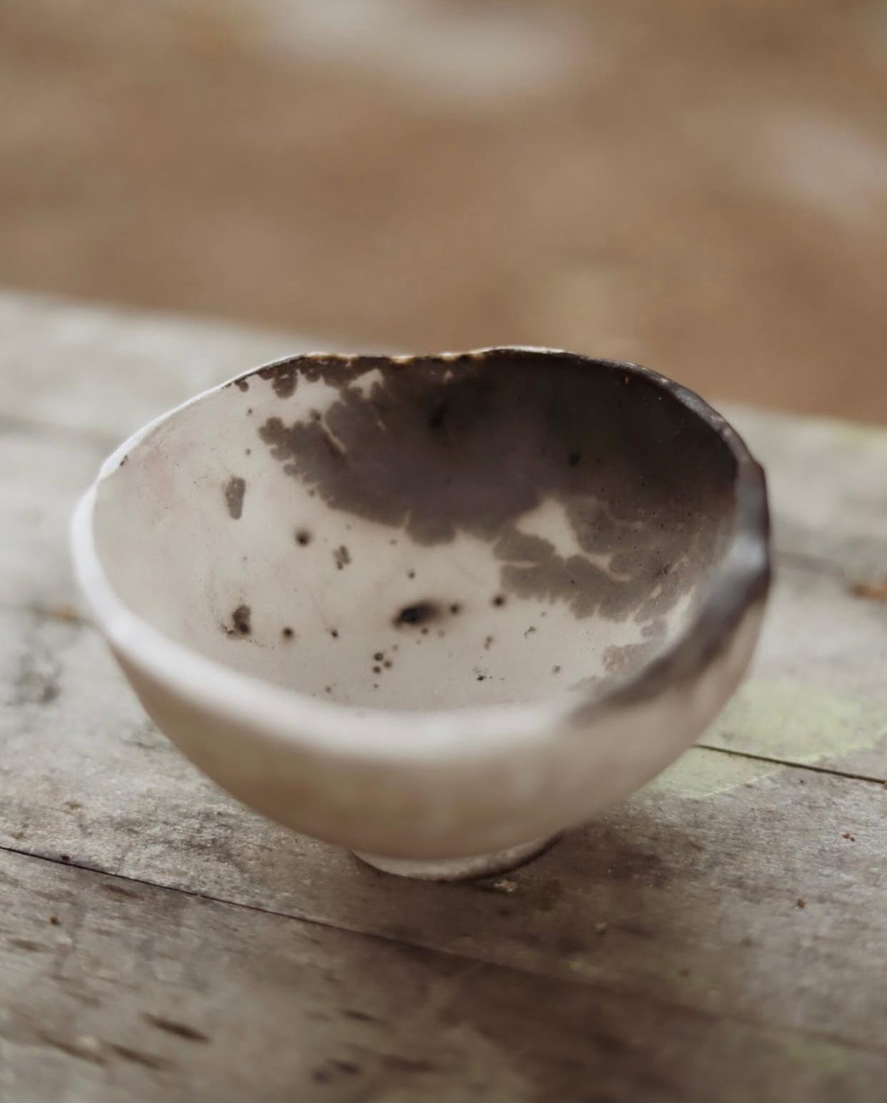 Bol petit de ceràmica artesanal clara amb vores irregulars i marques fosques naturals de fum, reposant sobre fusta rústica.