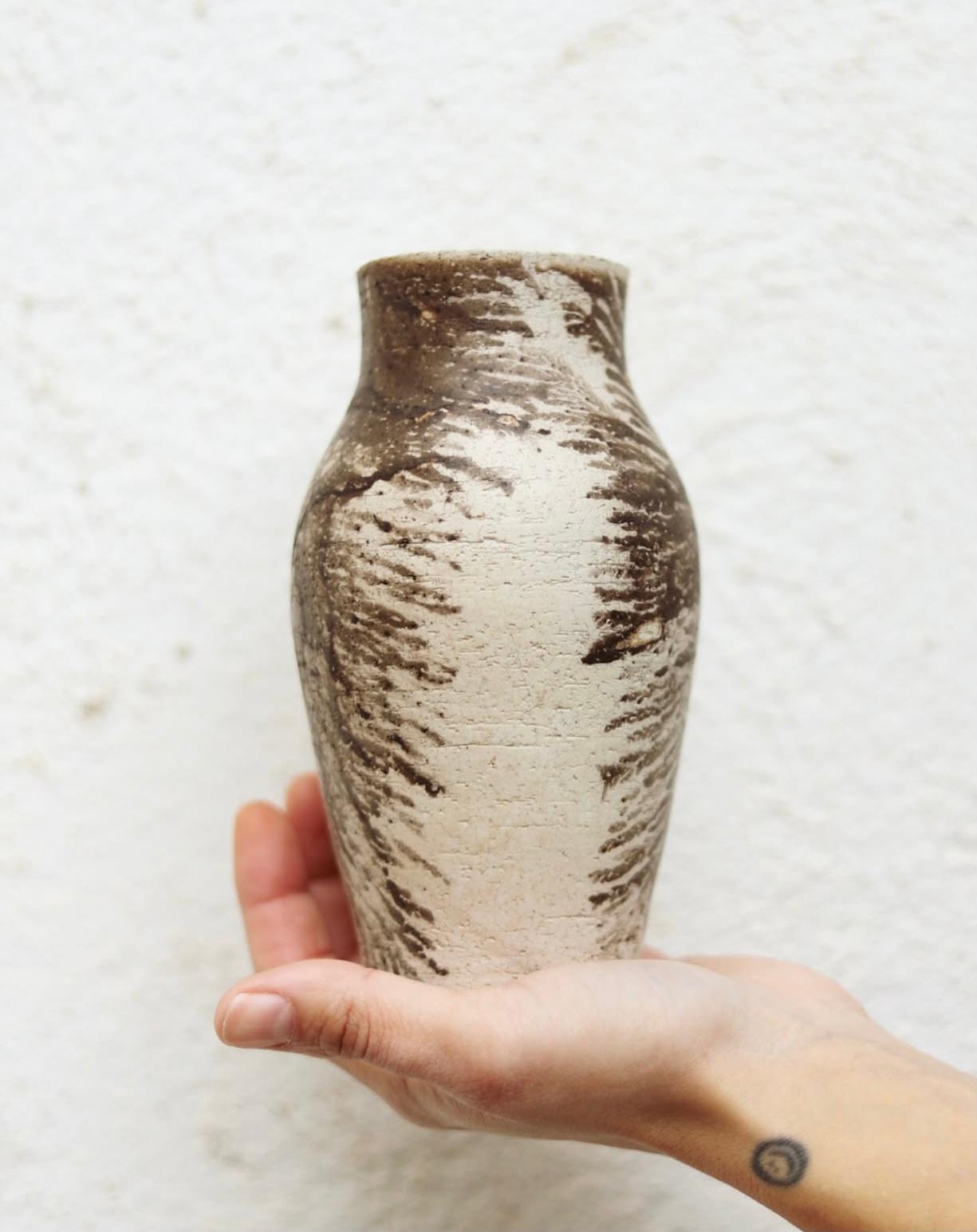 Mà sostenint un gerro de ceràmica artesanal amb textura estriada molt marcada i contrastos rústics de color clar i fosc.